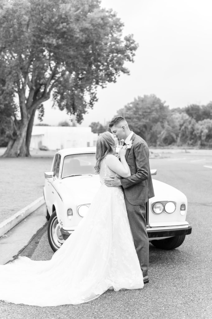 Black and white photo of the bride and groom kissing to celebrate their marriage in front of retro car at Royal Gorge Route Railroad