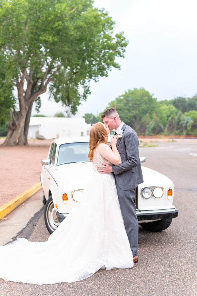 Wedding photo of the bride and groom kissing to celebrate their marriage in front of retro car at Royal Gorge Route Railroad