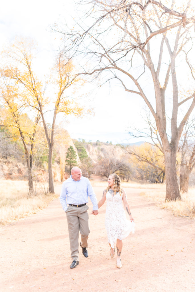 Couple walking holding hands under fall tree landscape at Red Rock Open Space 