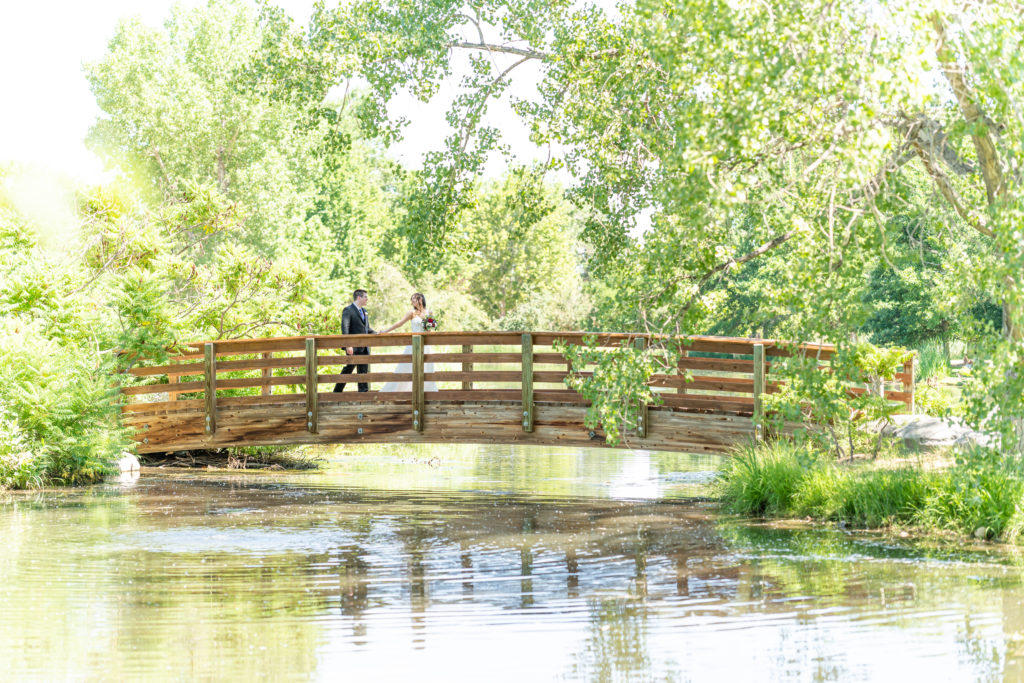 Bride and Groom walking across bridge at the Hudson Gardens and Event Center Wedding Venue in Littleton, Colorado.