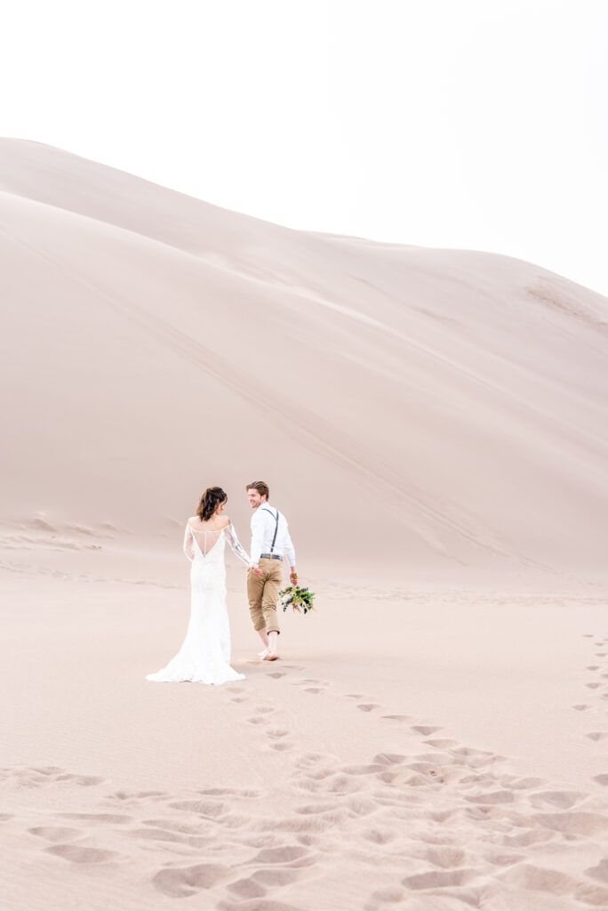 Groom holding his bride's hand walking out into the sand dunes landscape