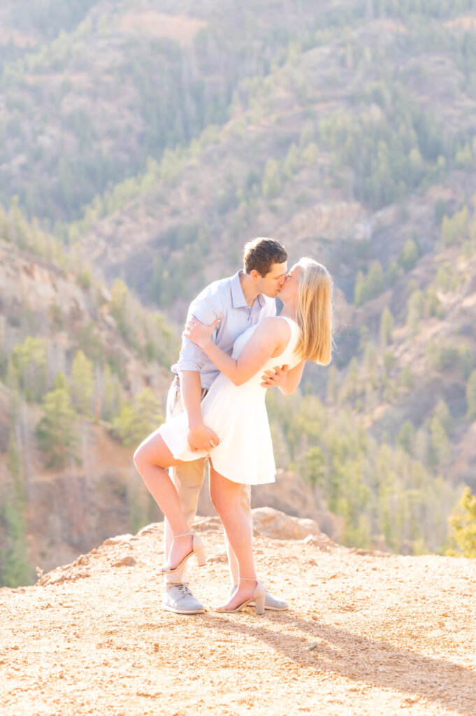 Couple going in for a dip kiss with the Colorado mountain range behind them for their Colorado Engagement Photos