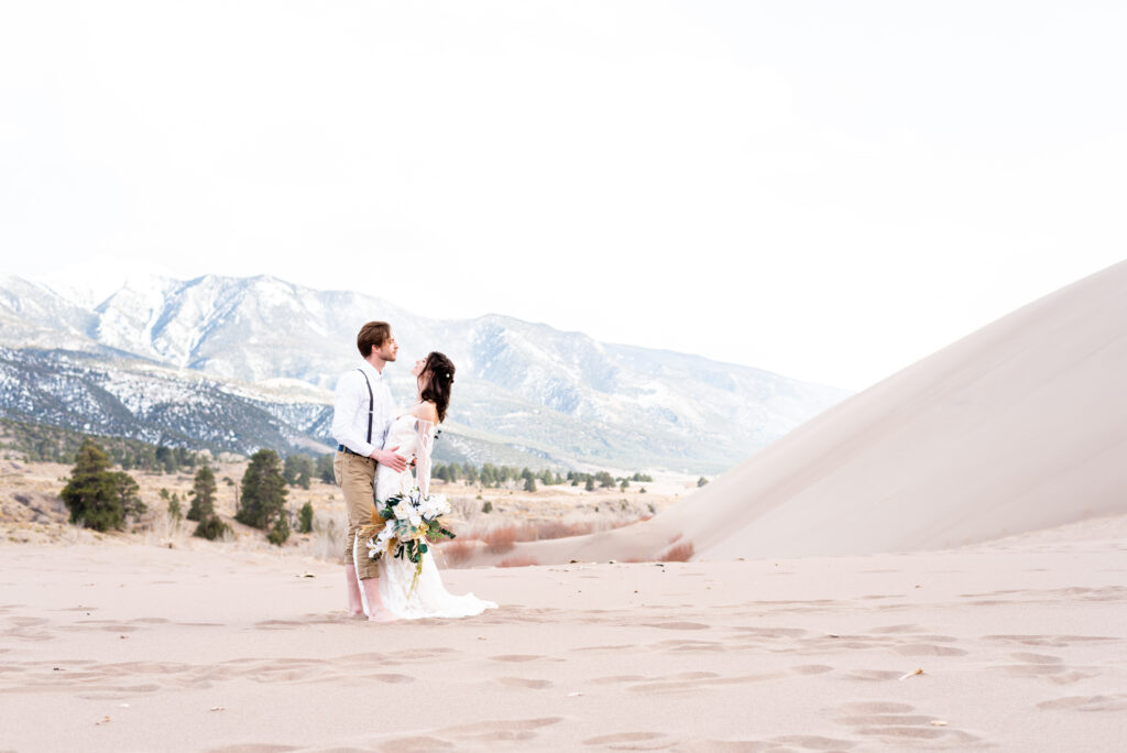 bride and groom hugging each other with great sand dune landscape behind them
