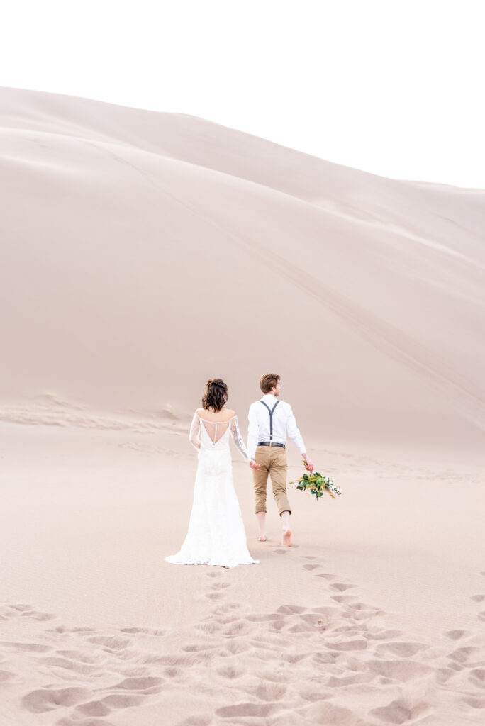 Bride and Groom holding hands walking out into the distance together in the dunes