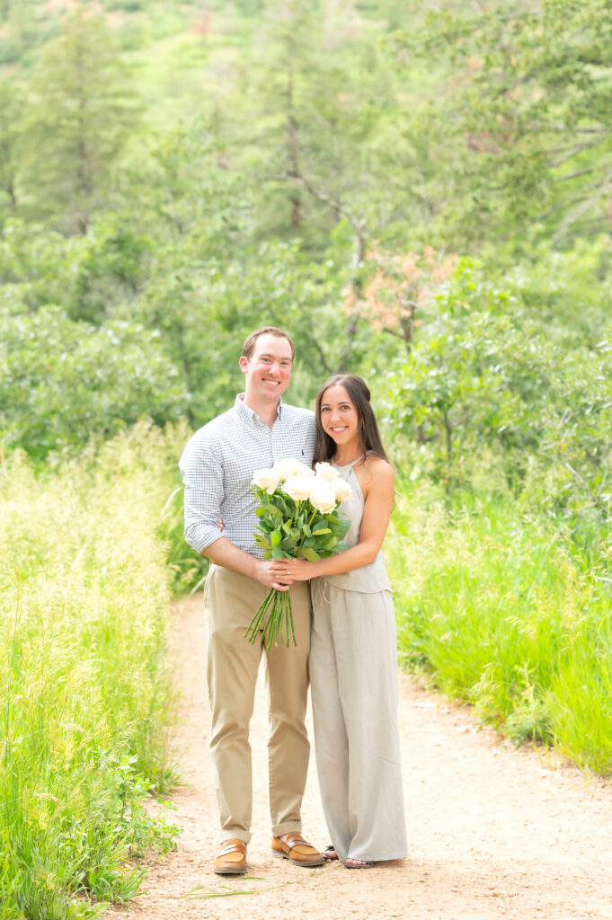 Couple smiling together holding bouquet of flowers to celebrate their engagement 