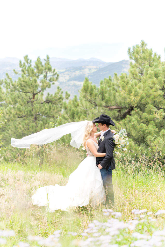 Bride and groom hugging one another in a beautiful wildflower field with mountain backdrop 