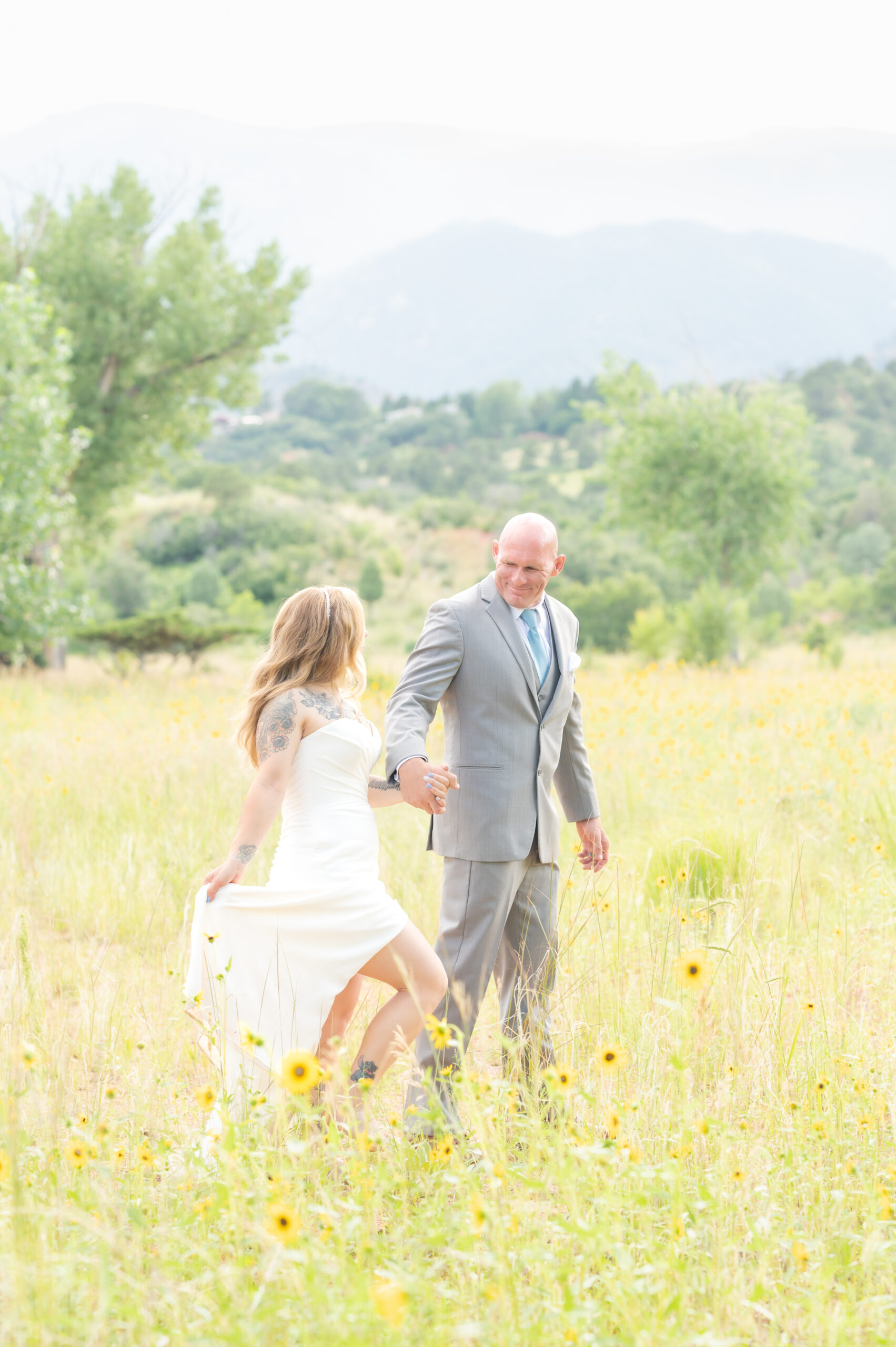 Couple in formal attire holding hands as they walk through a field of sunflowers in Colorado Springs