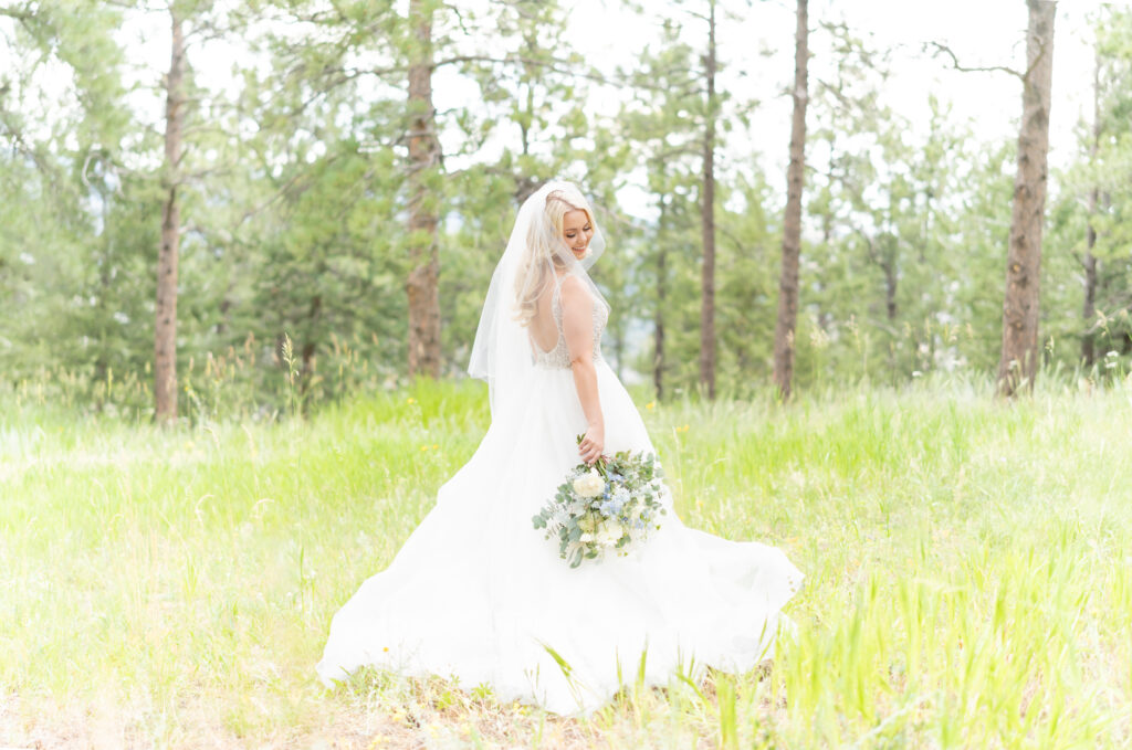 Beautiful portrait of the bride standing in open meadow while smiling over her shoulder holding her bridal bouquet