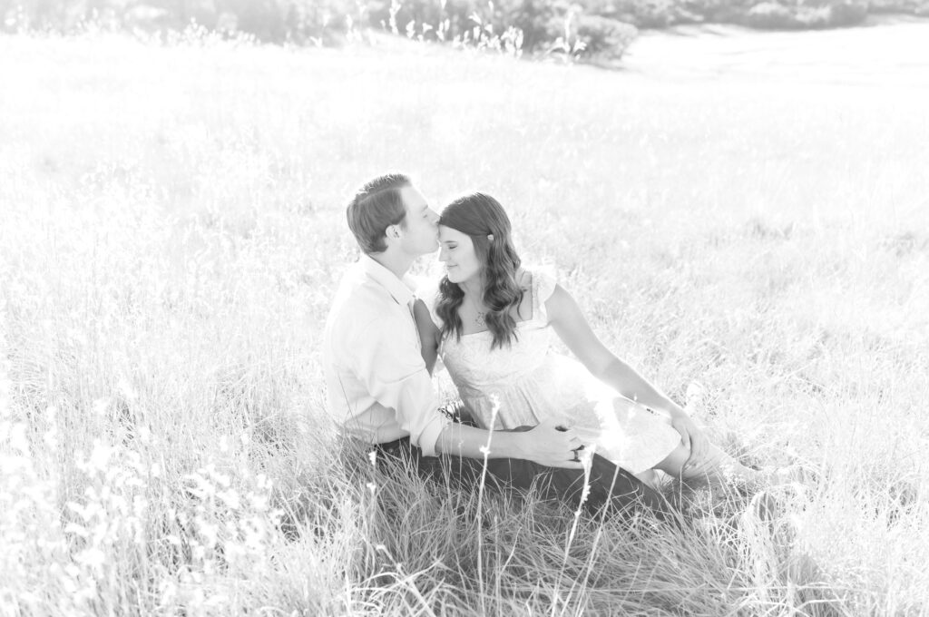 Couple kissing while sitting down together in an open meadow field at Dawson Butte Open Space in Colorado