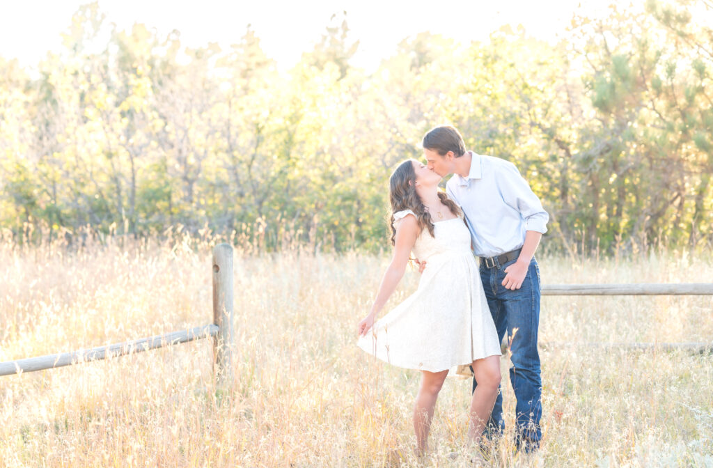 Couple going in a for a dip kiss in the open field while she is holding the edge of her dress
