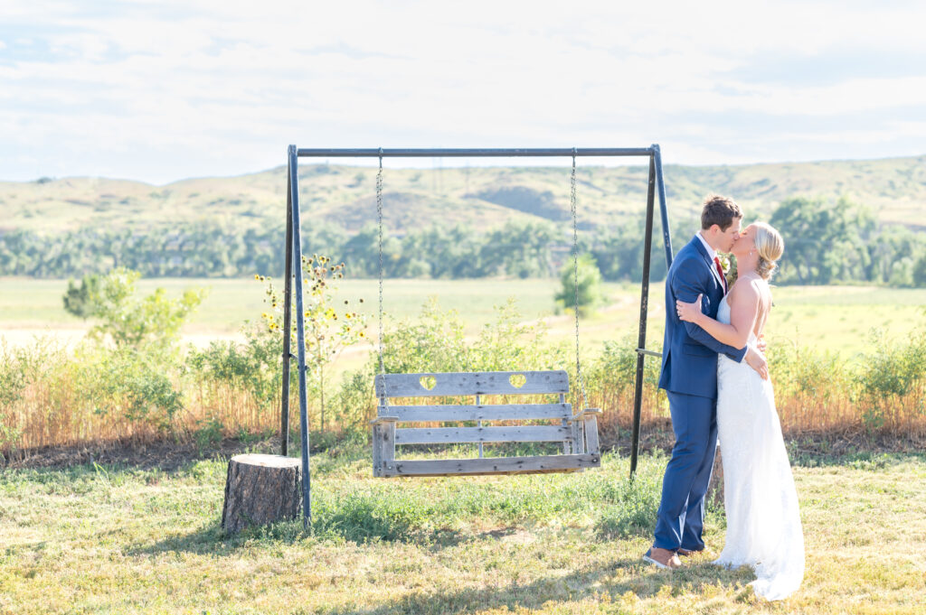 Bride and Groom kissing next to a swing outside on the open field at Venetucci Farm wedding venue in Colorado Springs