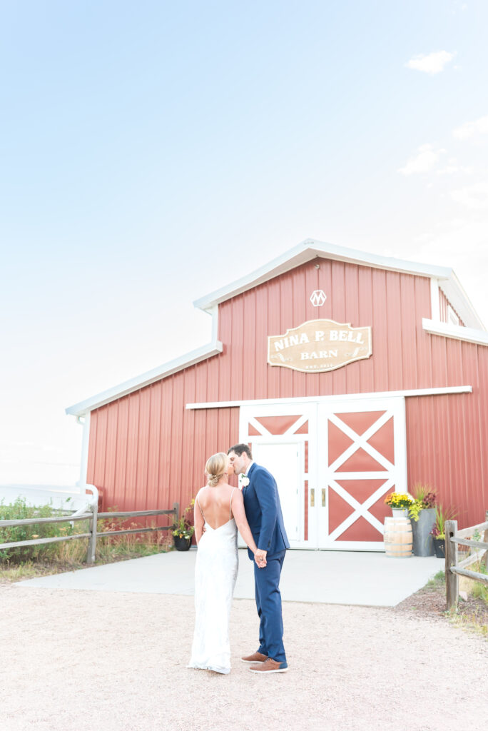 Bride and groom kissing while holding hands with barn landscape behind them at Venetucci Farm