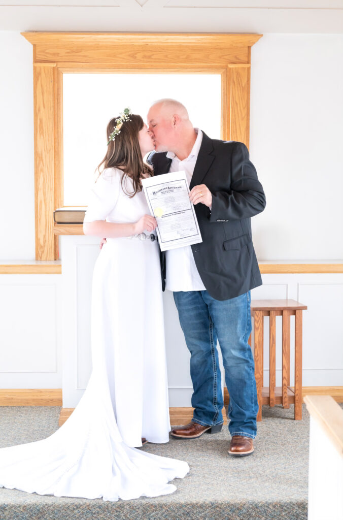 Bride and Groom kissing while holding their marriage license together inside American Mother's Chapel in Colorado Springs
