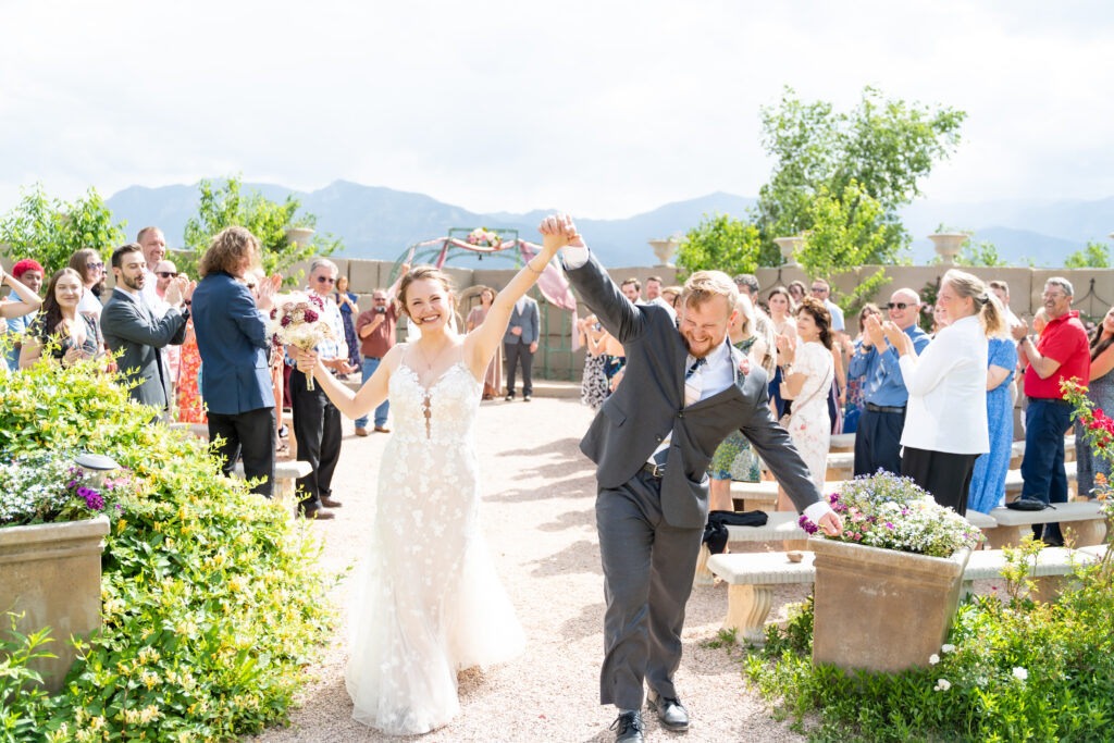 Bride and Groom holding hands in the air to celebrate their marriage as they walk down the aisle at Hillside Gardens and Event Center in Colorado Springs