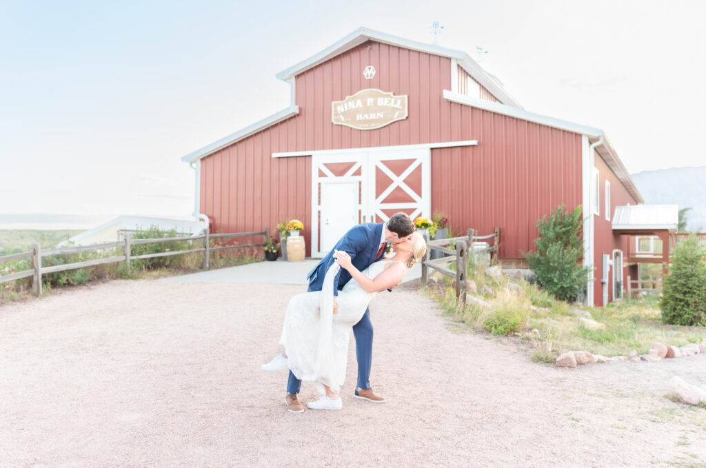 Groom dipping his bride for a kiss in front of the rustic barn at Venetucci Farm Wedding Venue