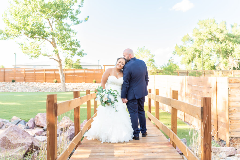 Bride and Groom coming in for intimate hug while standing on bridge at Creekside Event Center in Colorado Springs