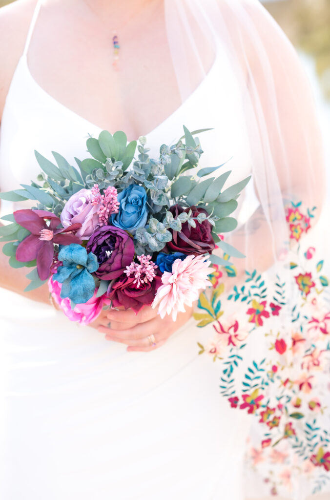 Bride holding her colorful bouquet against her dress on her colorado elopement day 
