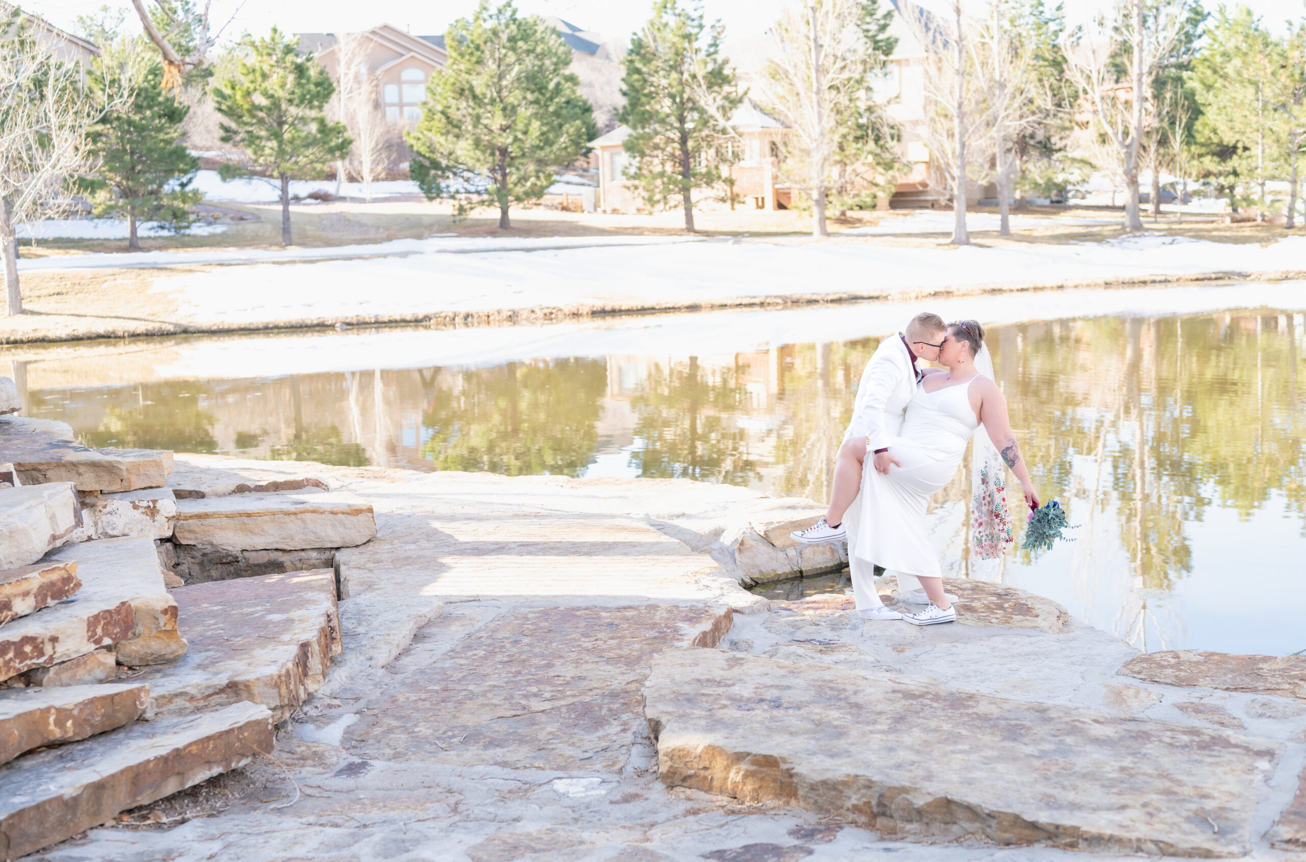 Bride dipping her bride for a romantic dip kiss with the pond view behind them to celebrate their Colorado Elopement Day