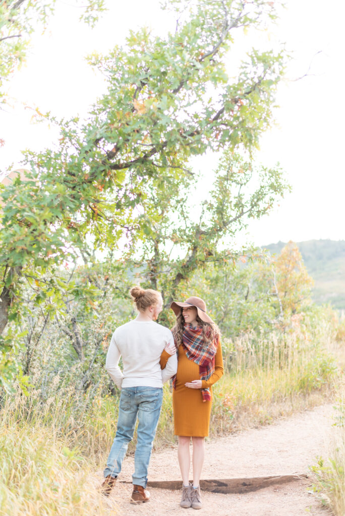 Man in jeans and white shirt links arms with his fiancee in an orange dress and plaid scarf during an engagement session in Colorado