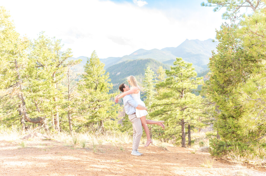 Man lifts woman into the air as they embrace against a mountain landscape in Colorado