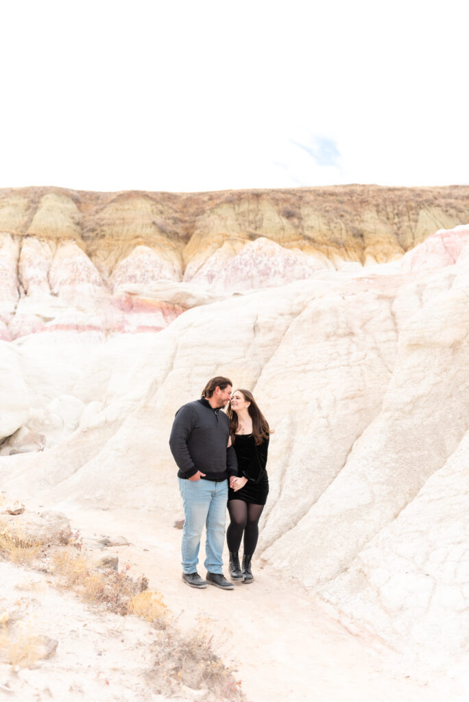 Man and woman hold hands and gaze lovingly into each other's eyes against a backdrop of white rock as they pose for engagement photos in Colorado