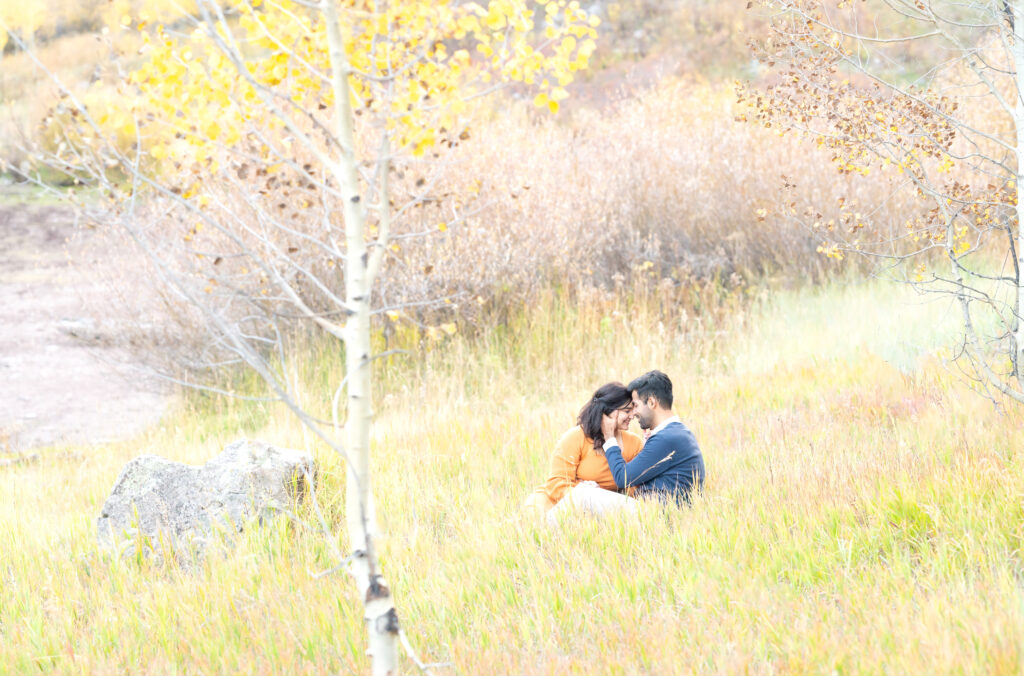 Engaged couple move in for a kiss as they sit together in a Colorado mountain meadow