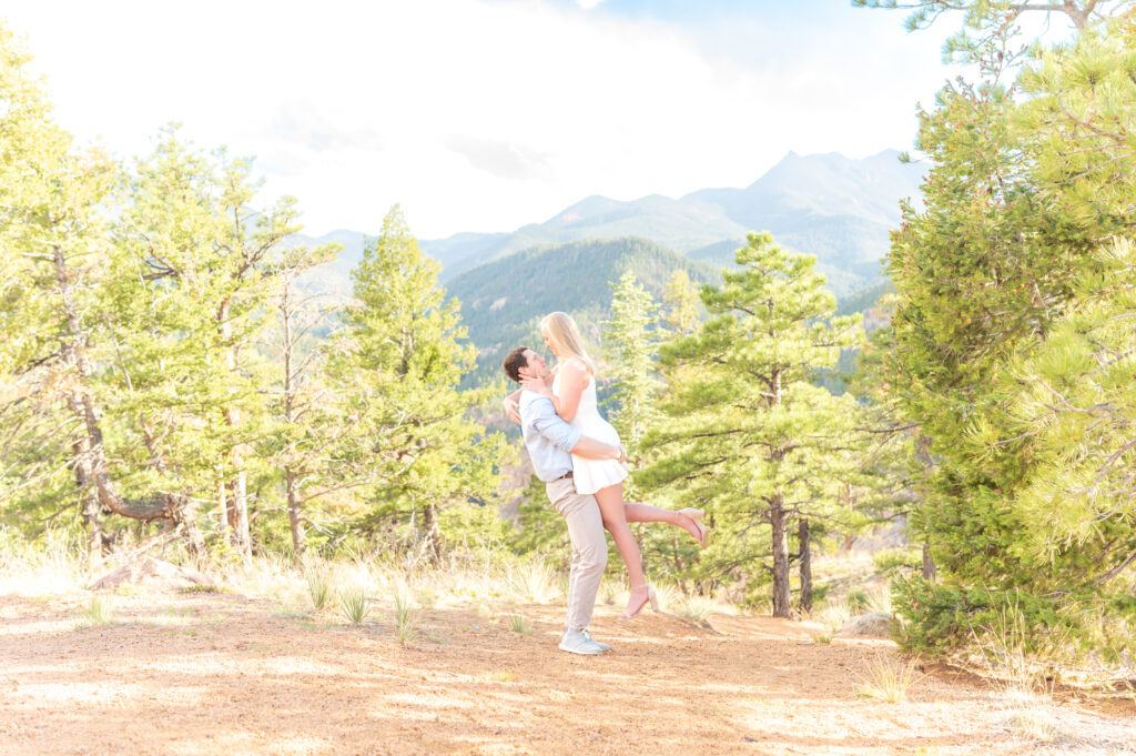 Man lifts his sweetheart into the air for a kiss along a wooded mountain path in CO