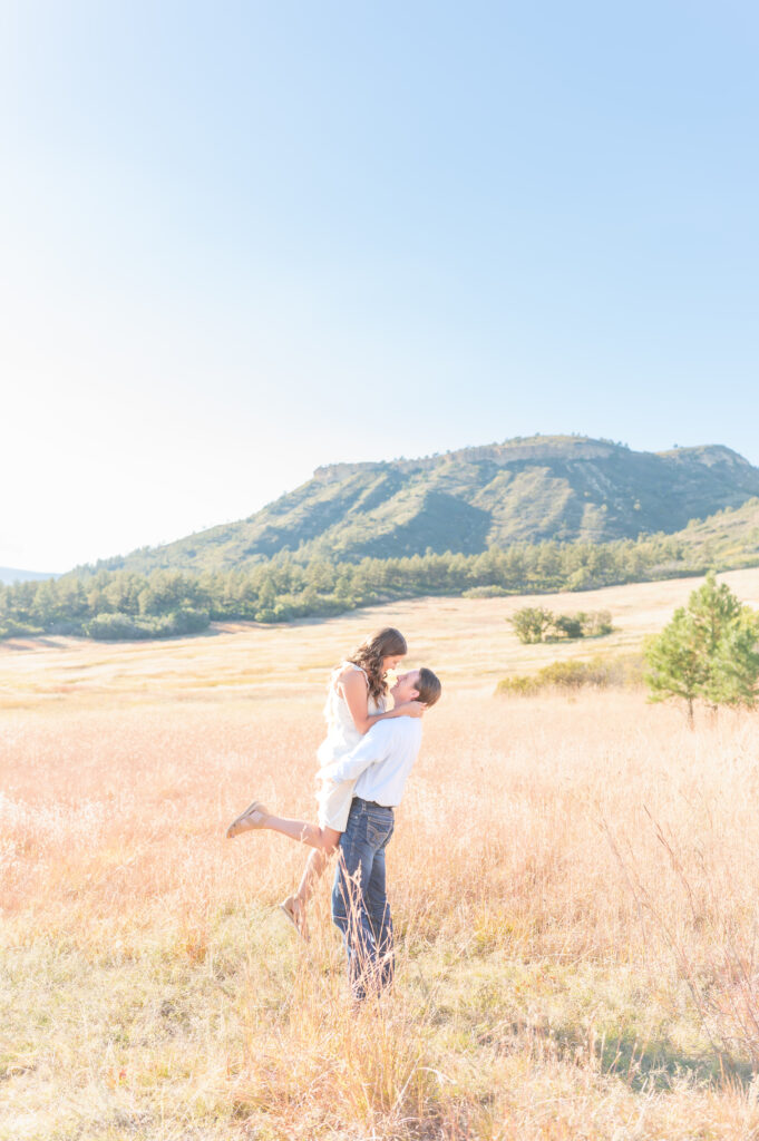 Stunning Colorado views provide a backdrop for a couple's engagement photo session as they pose in a sunny field
