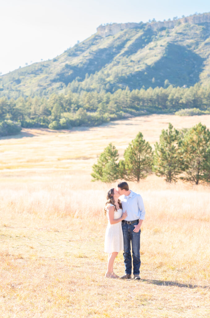 Woman in white sundress and man in jeans and a button-up shirt exchange a kiss during their Colorado engagement session