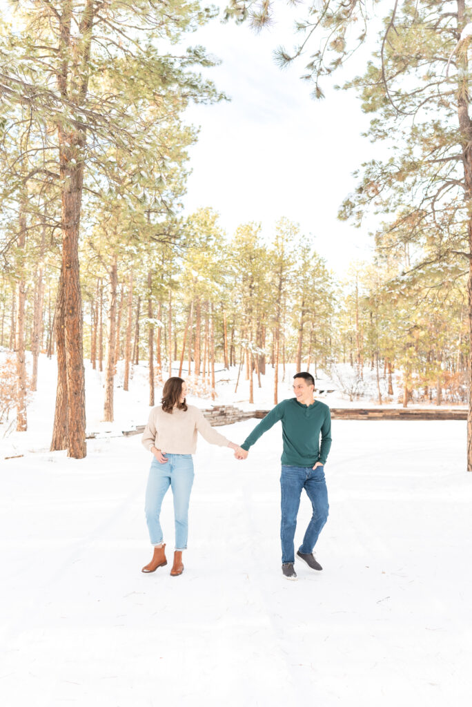 Couple in jeans, boots, and sweaters pose for engagement photos in a snowy woodland setting in Colorado