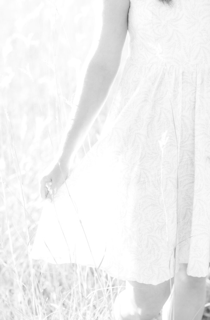 What to wear for your Colorado engagement session, close-up of woman's hand as she holds out the skirt of her sundress against sunlit meadow grass