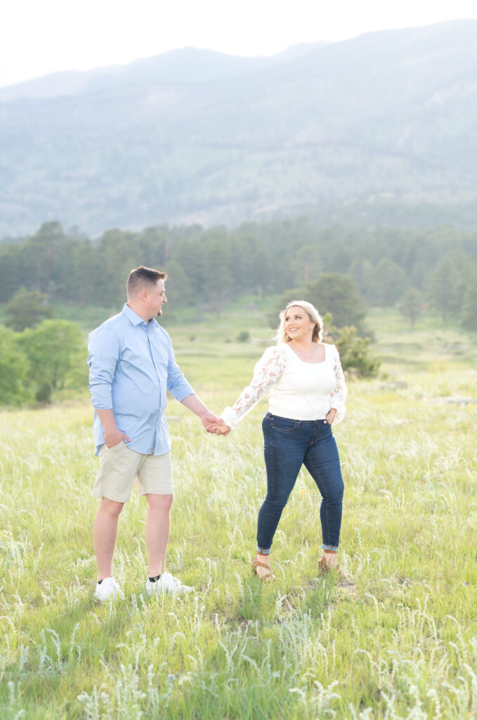 Young couple stroll through a Colorado meadow hand in hand during their engagement portraits