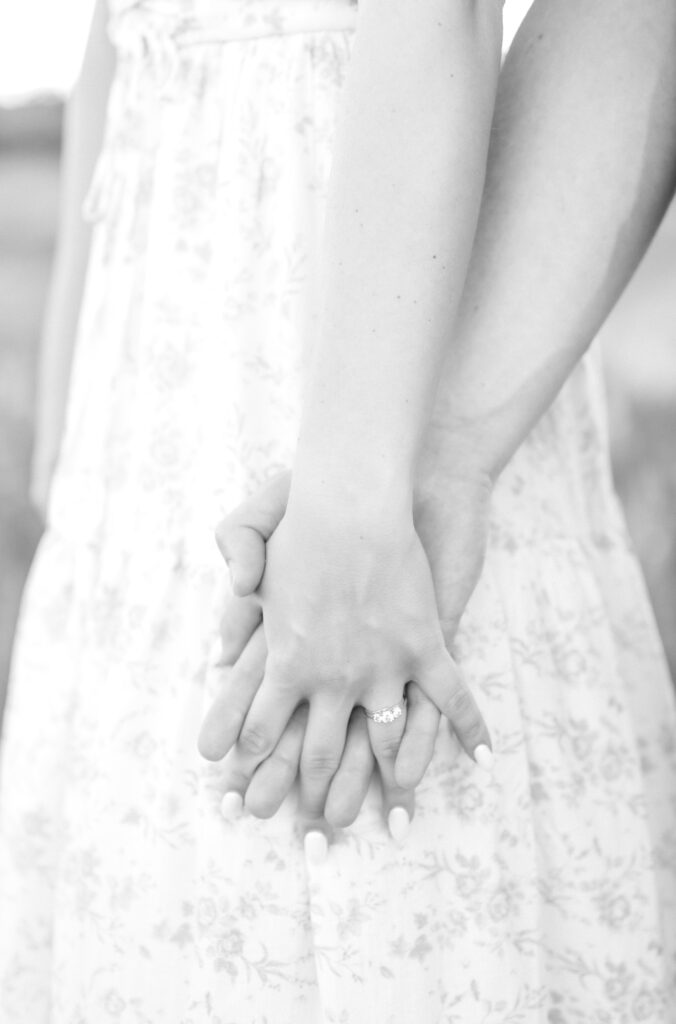 Detail black and white photo of couple holding hands and showing engagement ring