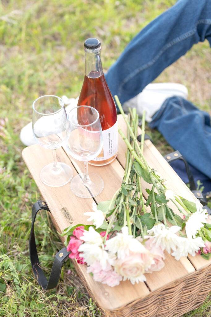 Picnic basket sitting on grass field with wine, wine bottles, and flowers sitting on top of the basket