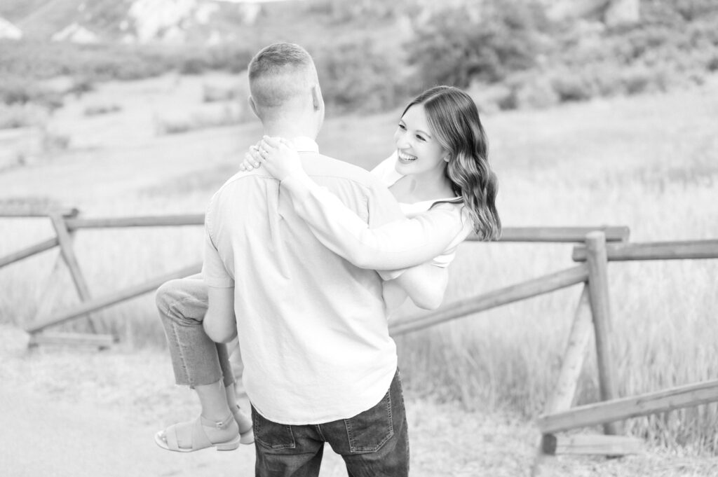 Young woman laughing as her husband picks her up and carries her along a fenced field in Colorado Springs