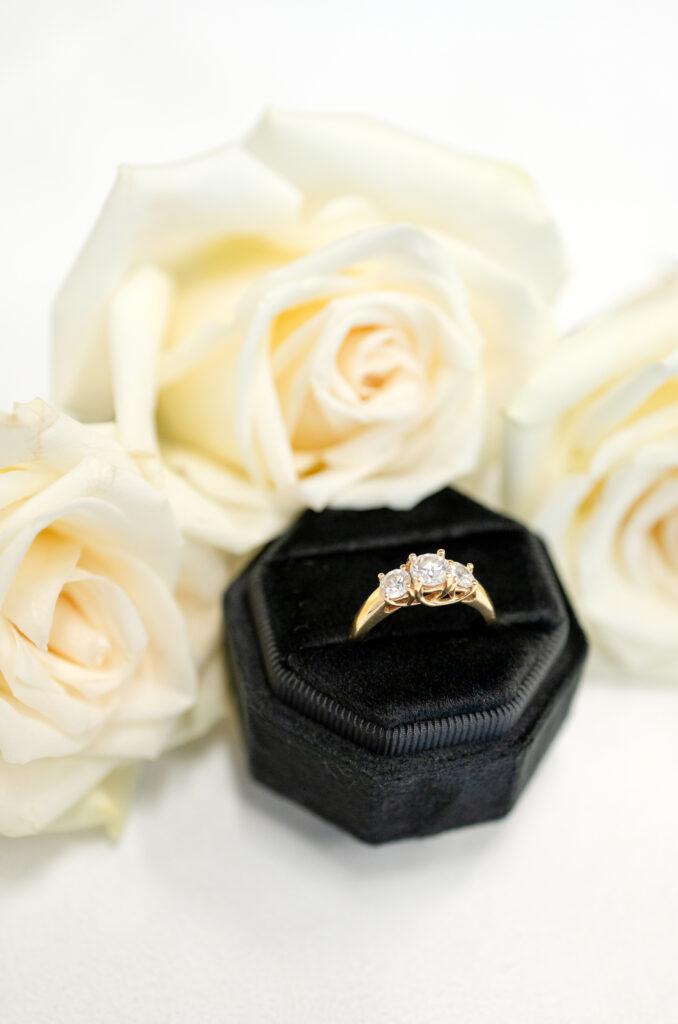 Detail of wedding ring in black velvet case surrounded by white roses