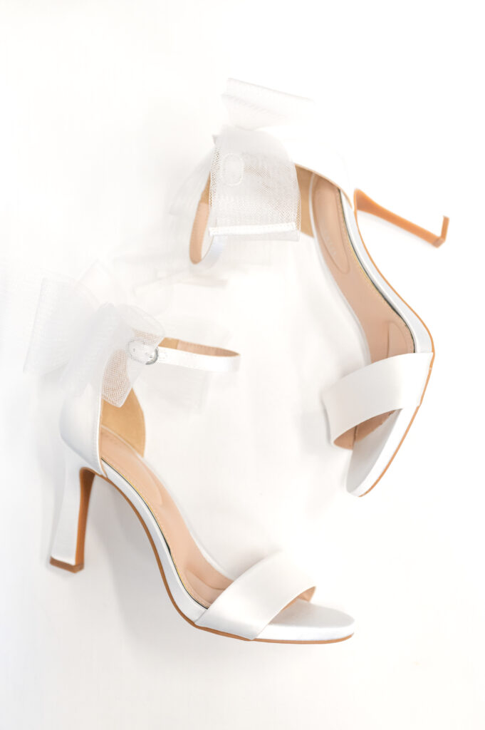 Bride's high-heeled shoes arranged with a flowing white ribbon. Tips for finding a wedding photographer.