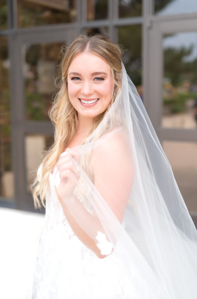 bride holding her veil while smiling towards the camera for her Colorado wedding