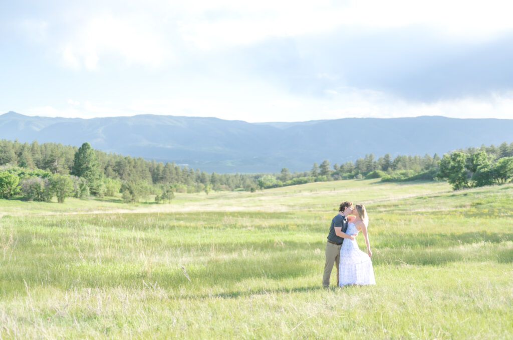 Couple kissing in an open meadow field with the mountain range behind them