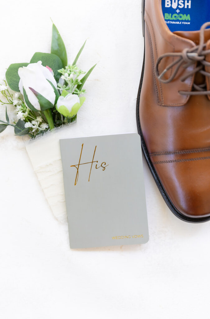 Detail wedding photo of the groom's shoes, his vow book, and his boutonniere