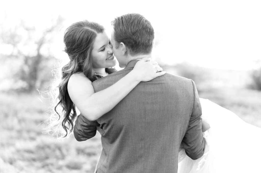 Black and white photo of the groom holding his bride while they both share an intimate moment caressing each other's nose