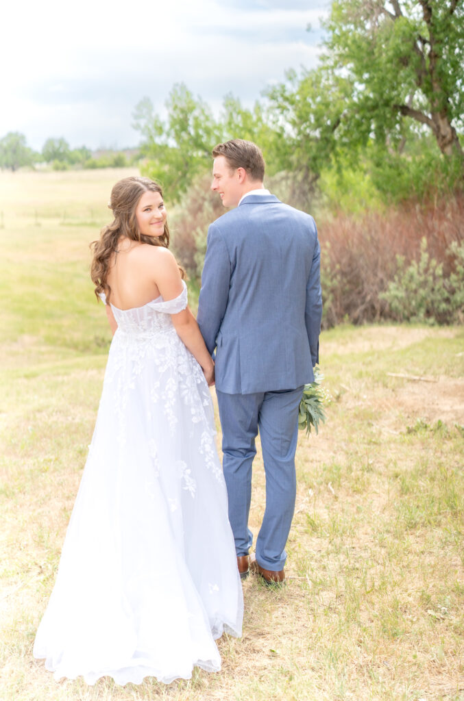 Bride and groom walking and holding hands while the bride is looking back and smiling at the camera 