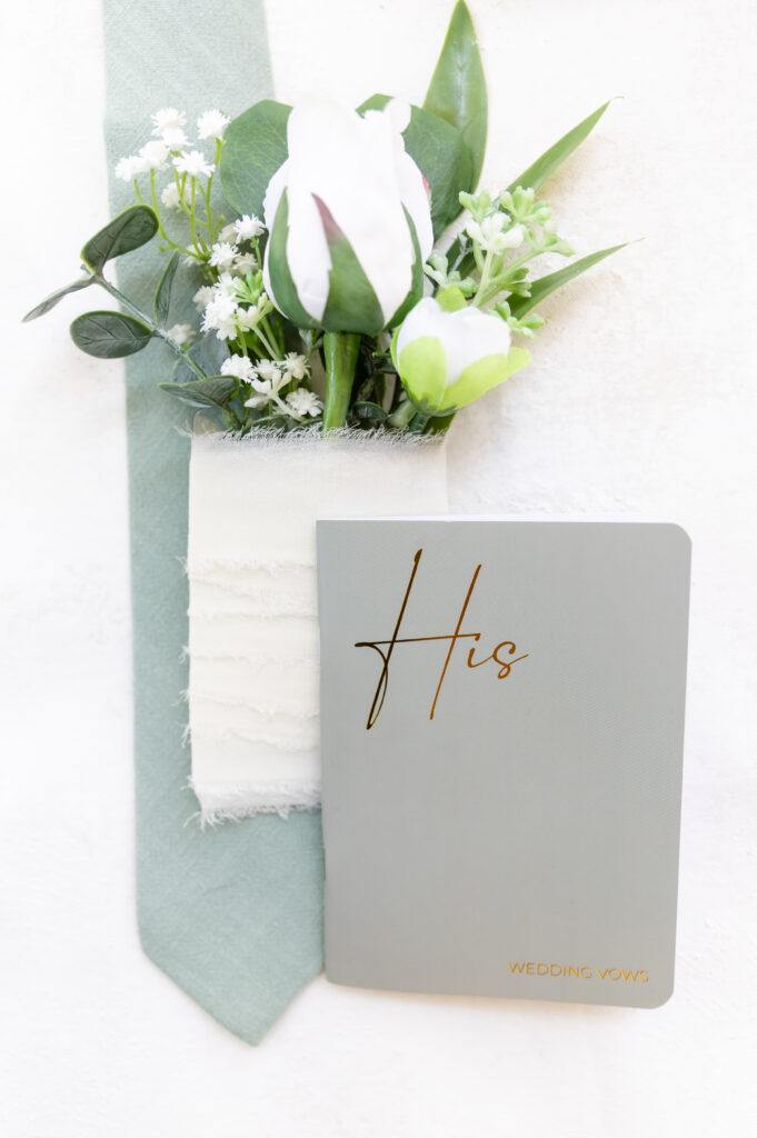 Photo of the groom's vow book laying on top of his boutonniere and tie 