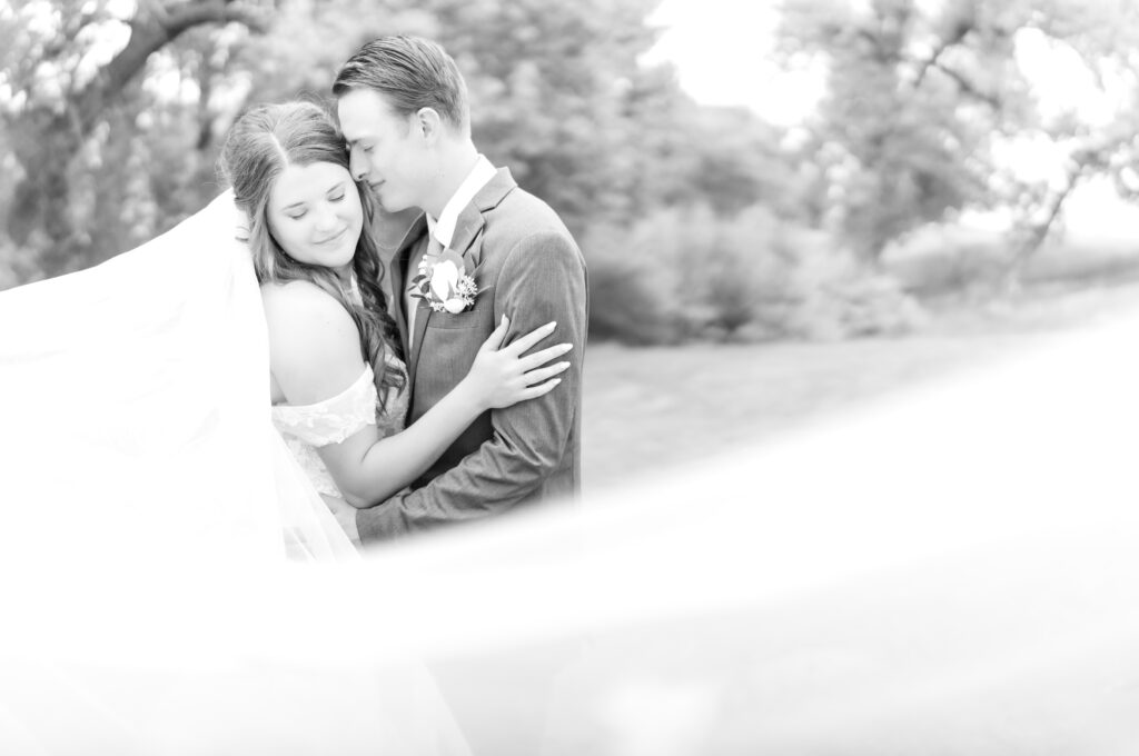 Groom looking at his bride while going in for intimate hug together with the bride's veil creating a beautiful foreground effect in the photo 