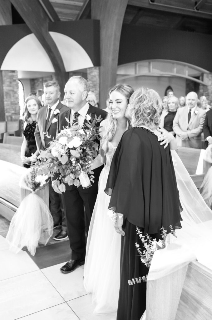 Bride's mother giving her a kiss on the cheek during their Catholic Church wedding ceremony 