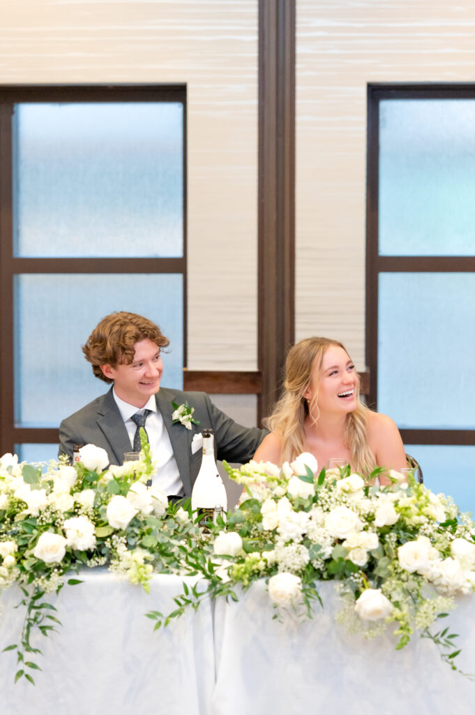 Bride and groom sitting at dinner table laughing during speeches at their wedding reception at The Denver Inverness Hotel 