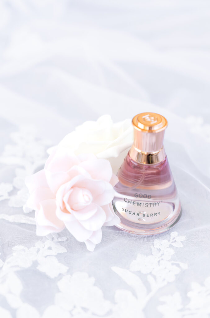 Detail photo of the bride's perfume sitting on the bride's veil with pink and white florals