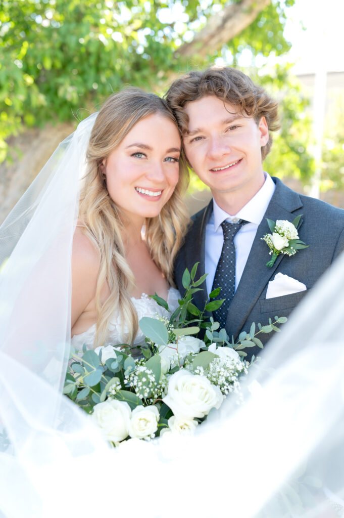 Bride and groom learning their heads together and smiling towards the camera with the bride holding her bouquet