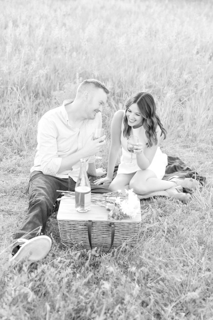 Black and white portrait photo of couple sitting in grass having a picnic and wine together at Roxborough State Park