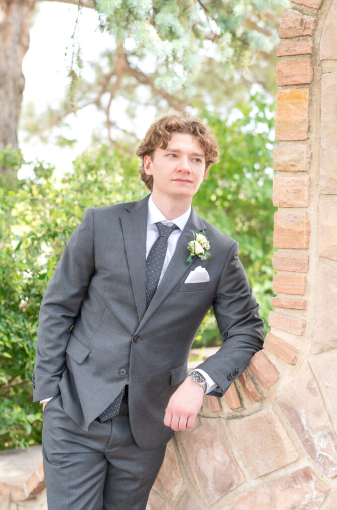 Groom leaning on brick wall while looking out into the distance 